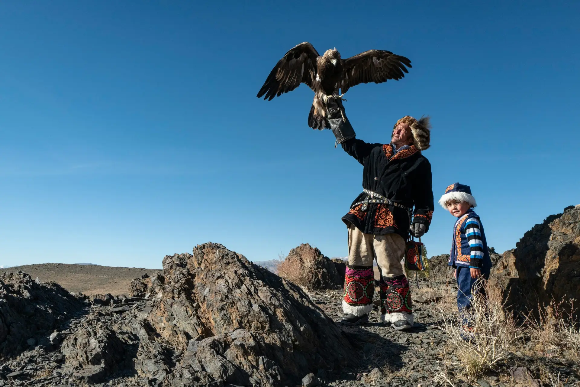 Homme en tenue traditionnelle tenant un aigle dans un paysage de Mongolie