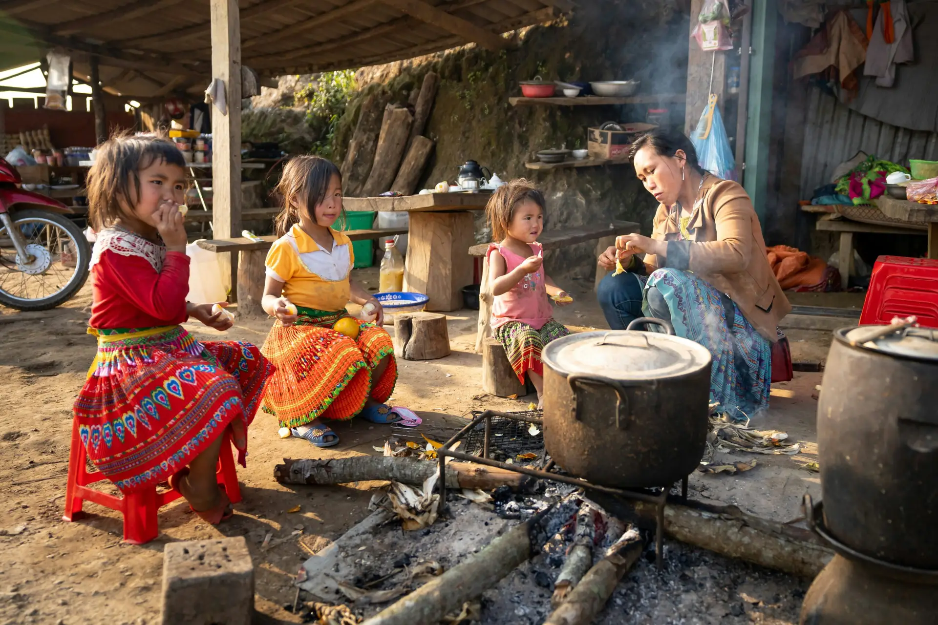 Femme préparant un repas avec plusieurs enfants autour d’un feu